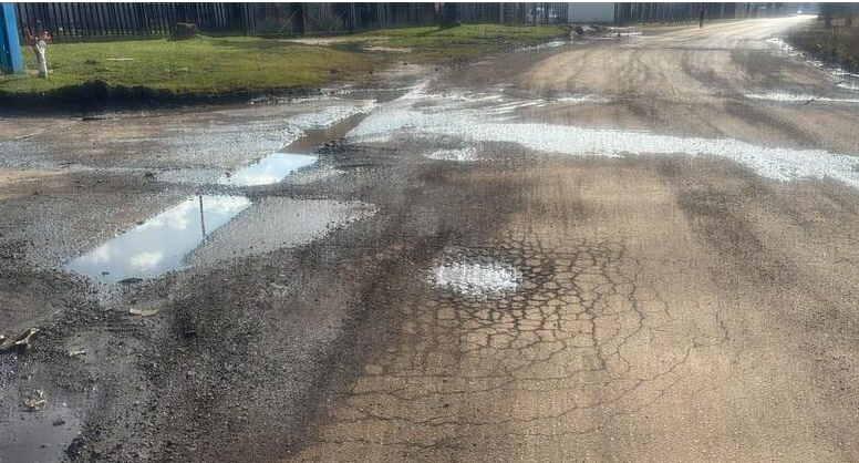  Deep cracks, potholes, and standing water cover a crumbling asphalt road surface in the Alrode industrial area.