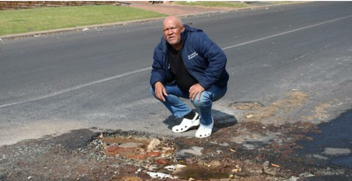 City of Ekurhuleni Ward 91 Councillor, Desmond Mckenzie standing next to a pothole with water leakage on a repaired Jukskei Road.