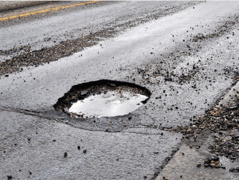 A large pothole filled with water on an asphalt road/