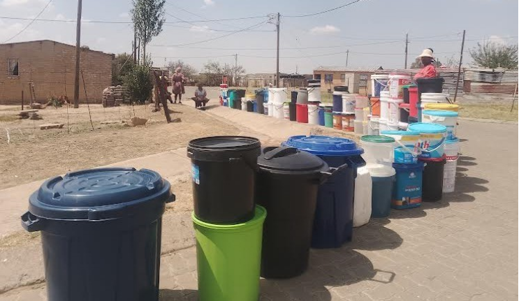 People leave their buckets in the queue waiting for the water truck.