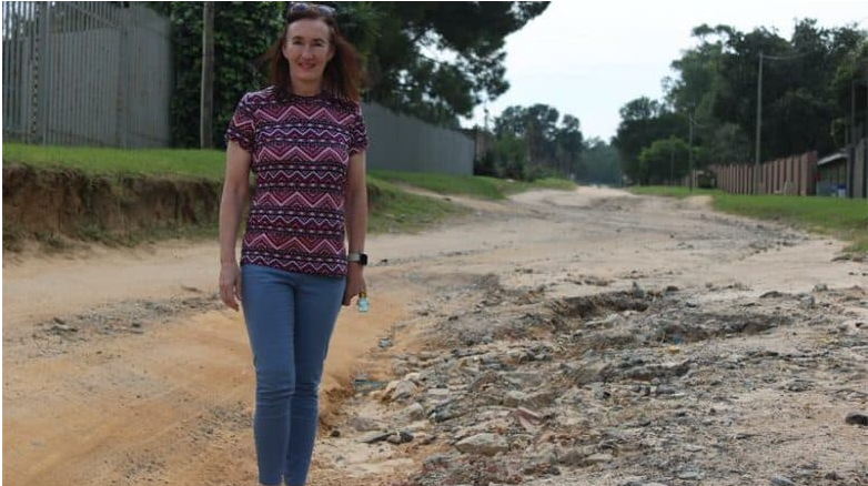 Shirley Bosman stands next to the deteriorated road